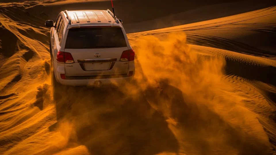 Toyota Land Cruiser 200 / V8, white SUV climbing a dune in blowing sand