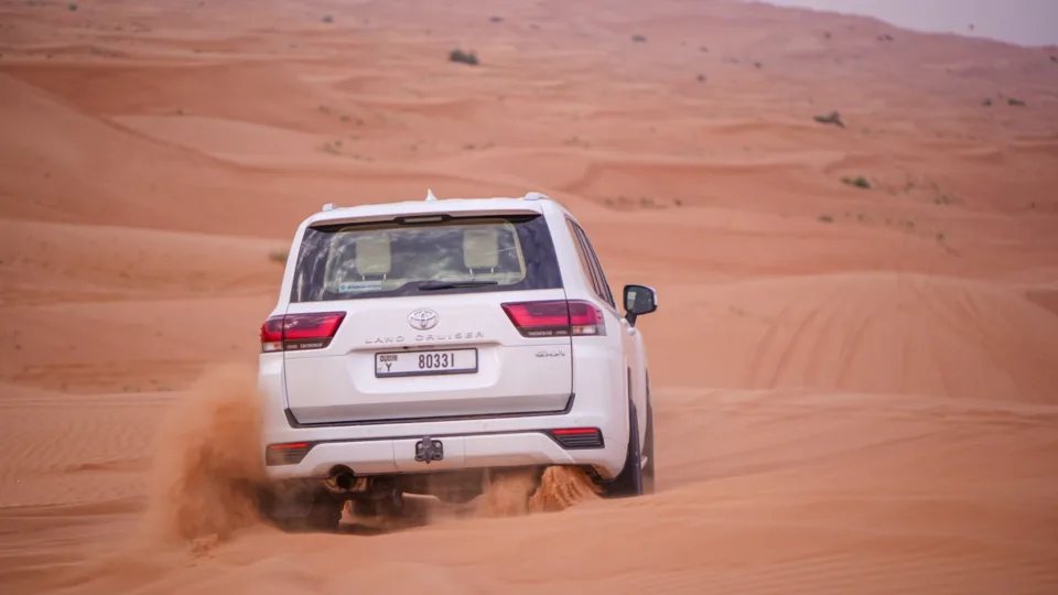 Toyota Land Cruiser 300, white SUV driving across desert sand, rear view